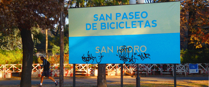 Las bicicletas pasean beatificadas, no así las gentes. Cartel con cromática de escaso contraste –una paradoja para vía pública– intervenido por los demonios urbanos de siempre.